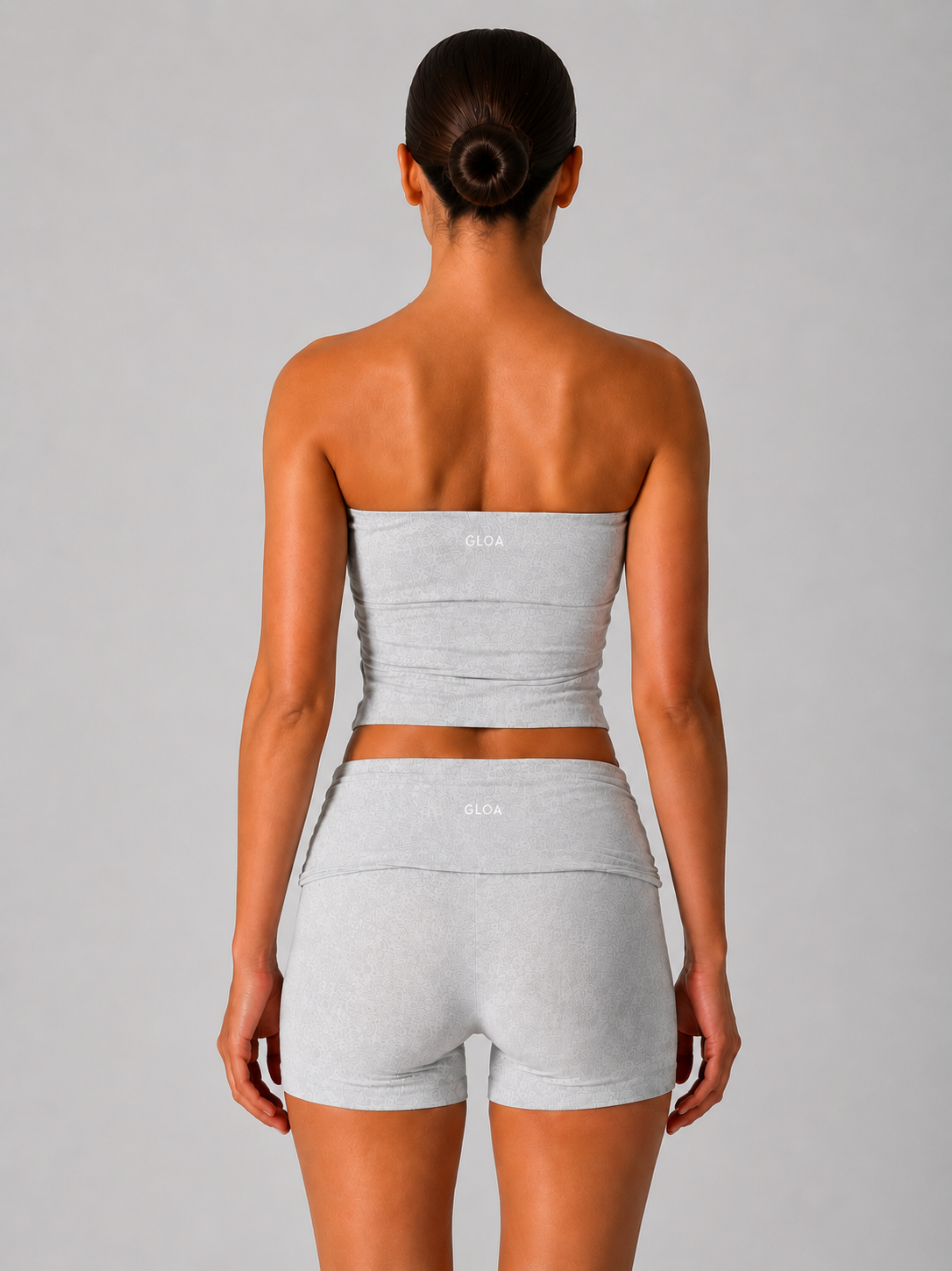 Woman wearing a gray strapless top and shorts set on a plain background