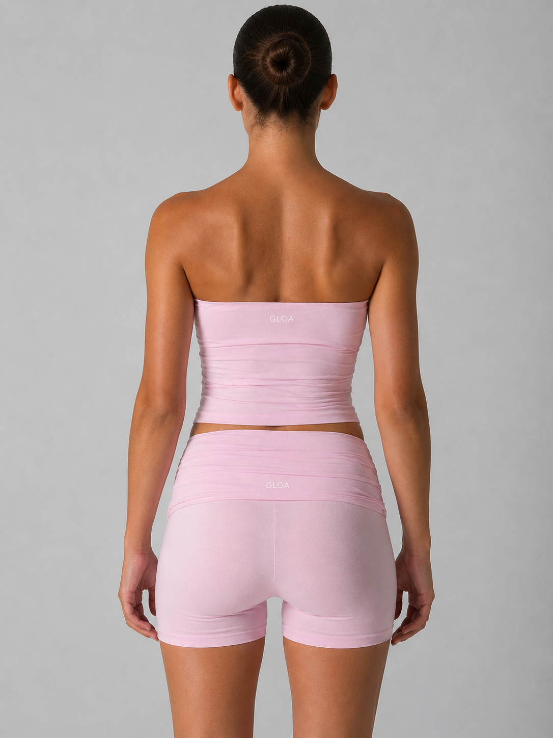Woman wearing a pink strapless top and shorts set on a gray background