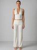 Woman wearing a white halter top and wide-leg pants against a gray background