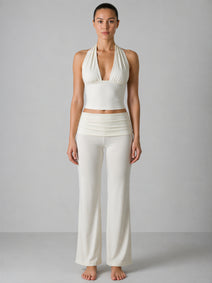 Woman wearing a white halter top and wide-leg pants against a gray background
