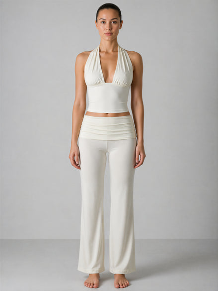 Woman wearing a white halter top and wide-leg pants against a gray background