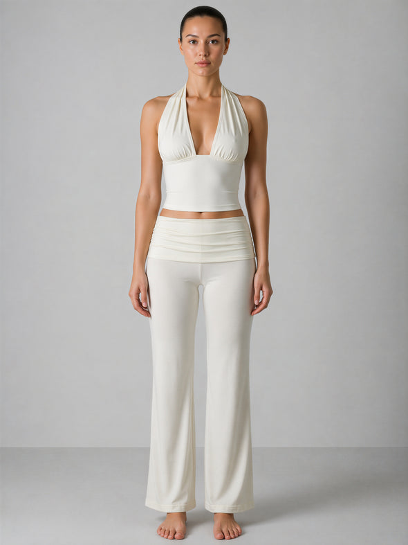 Woman wearing a white halter top and wide-leg pants against a gray background