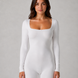 Woman wearing a white long-sleeve bodysuit against a gray background